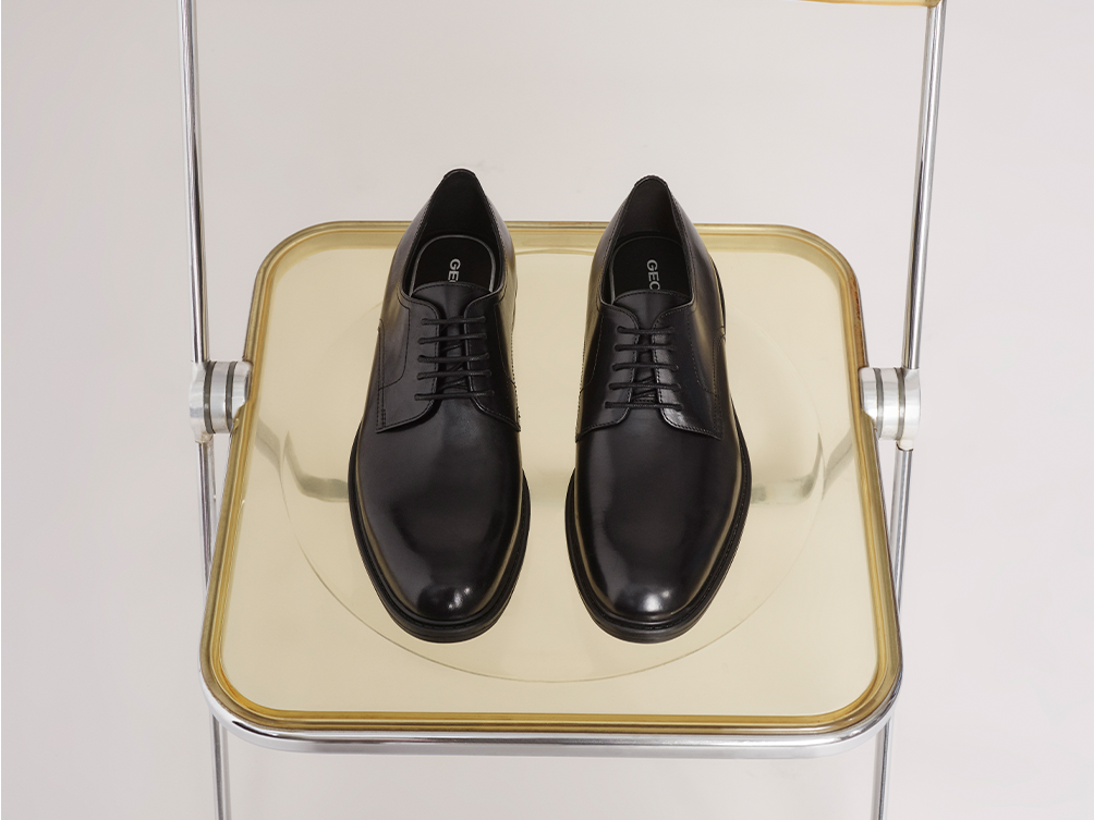 Man sitting on a blue sofa wearing a grey suit and resting black leather Chelsea boots on pink carpet | GEOX | GEOX