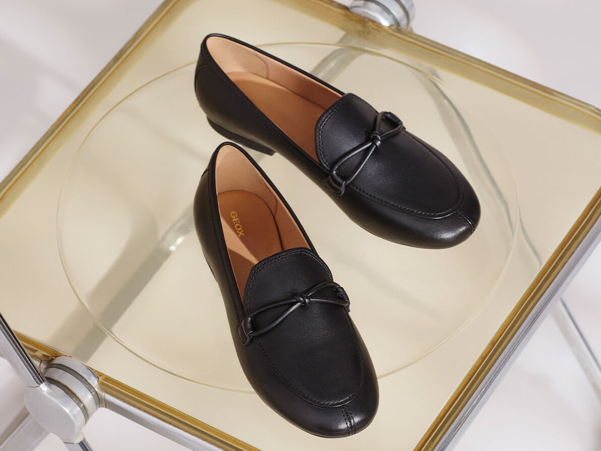 Sneaker in pelle lucida una nera poggiata su lampada e una marrone su scrivania in acciaio con orologio sullo sfondo che segna le ore 19:24 | GEOX | GEOX
