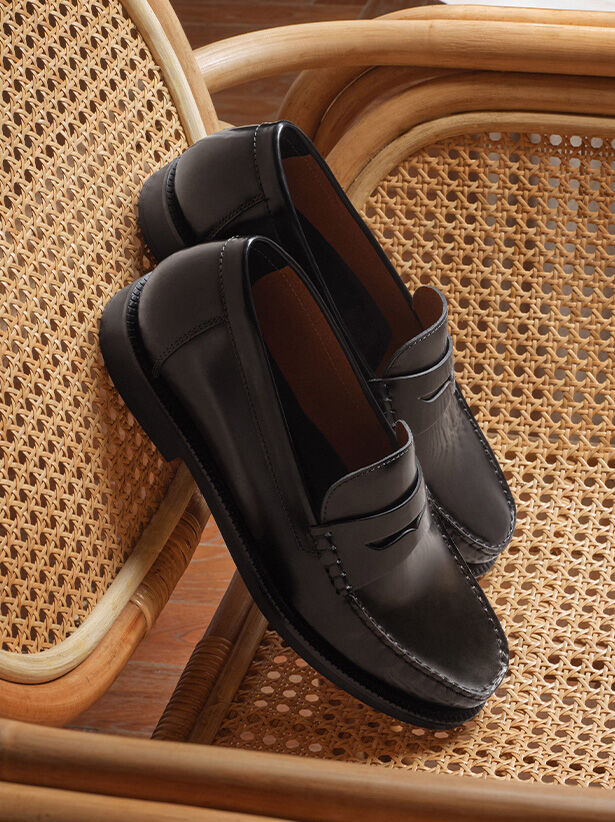 Pair of black leather loafers for men standing on their tips against the back of a wicker chair with parquet flooring in the background |GEOX | GEOX